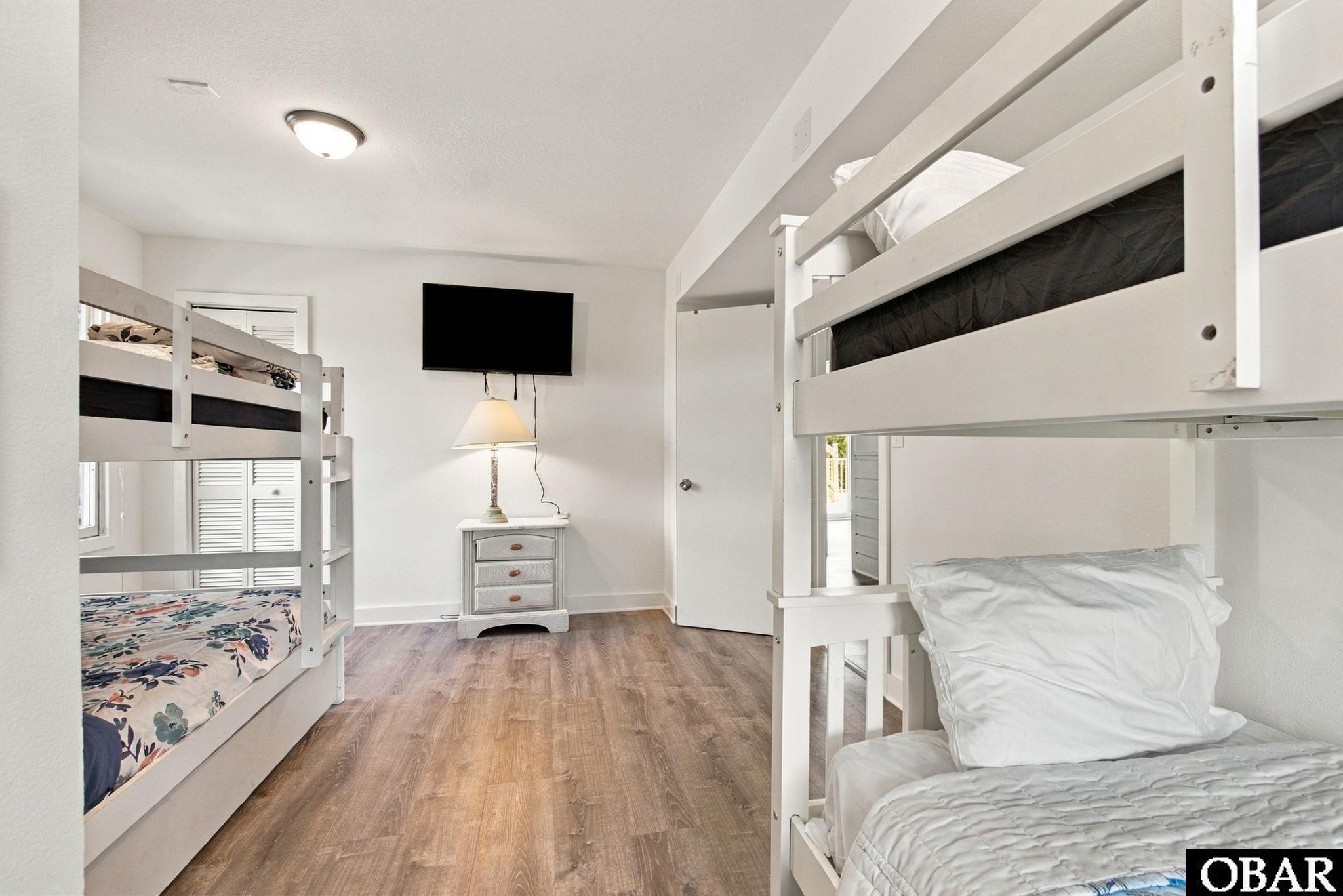 Bedroom with white bunk beds, wood-look flooring, and a wall-mounted television.