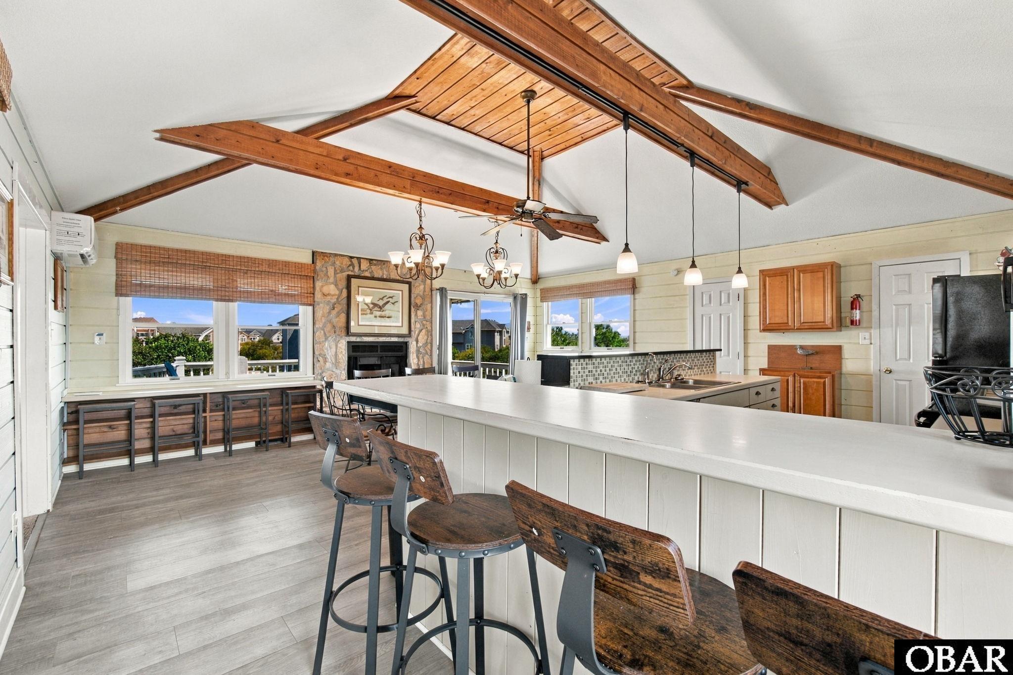 Kitchen with a long white island, wood-beamed vaulted ceiling, and stone fireplace.