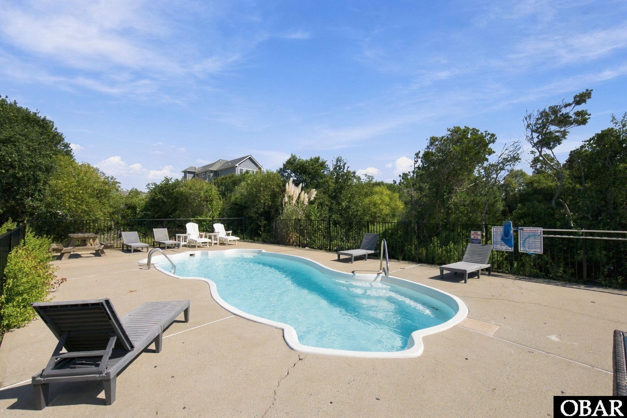 Outdoor pool with a curving shape, lounge chairs, and trees around the deck.