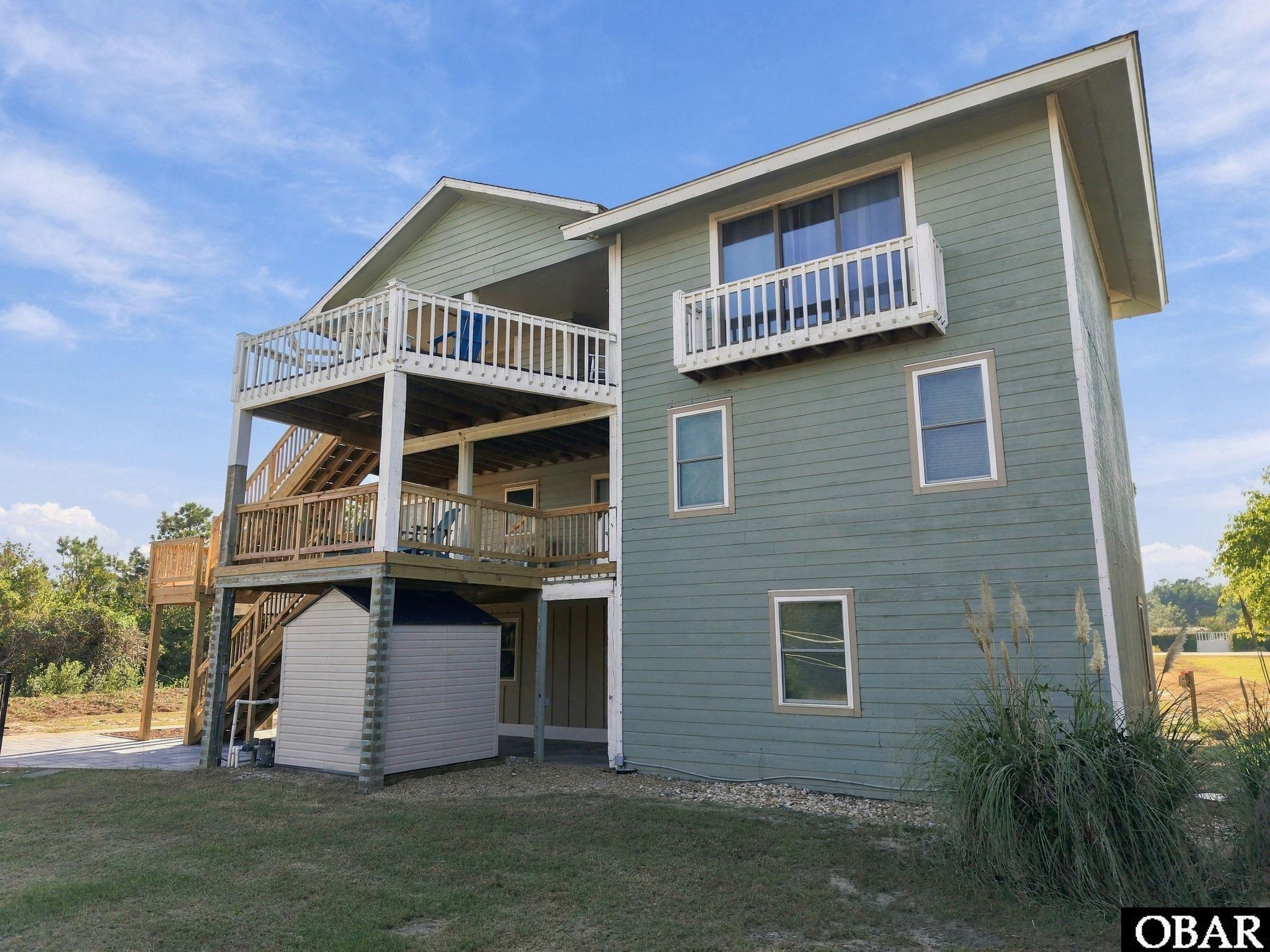 Sage-green two-story house with elevated wooden decks and exterior stairs.
