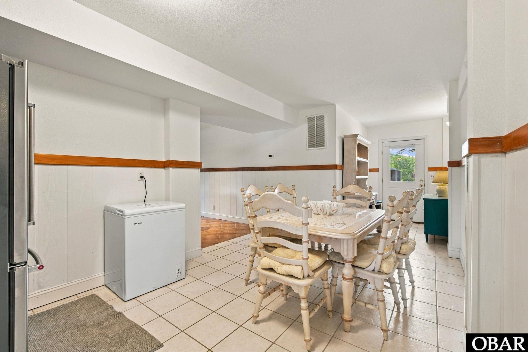 Dining area with a white table and chairs, chest freezer, and tiled floor.
