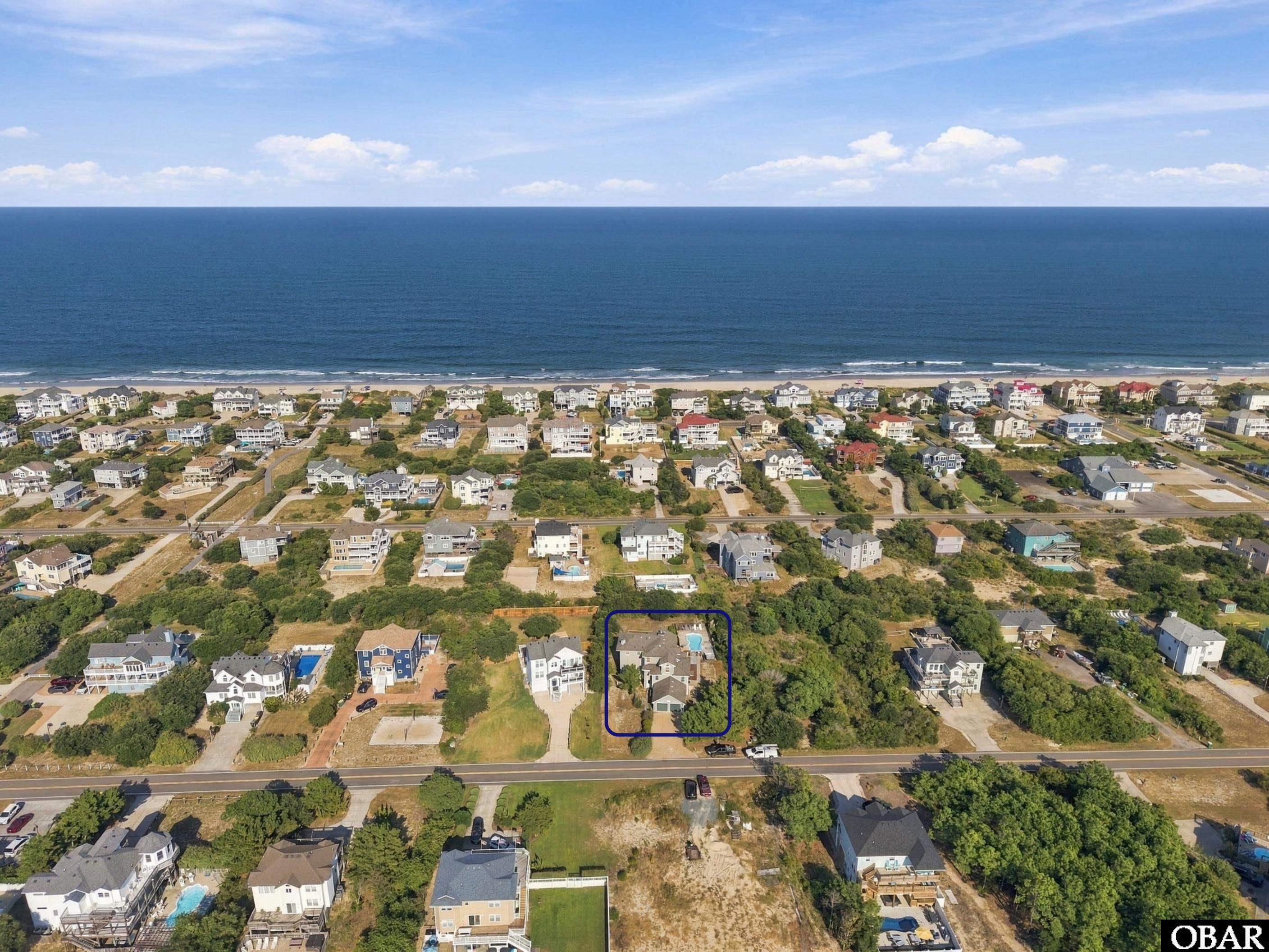 Aerial view of the outlined house among Corolla homes, with a pool and the ocean beyond.