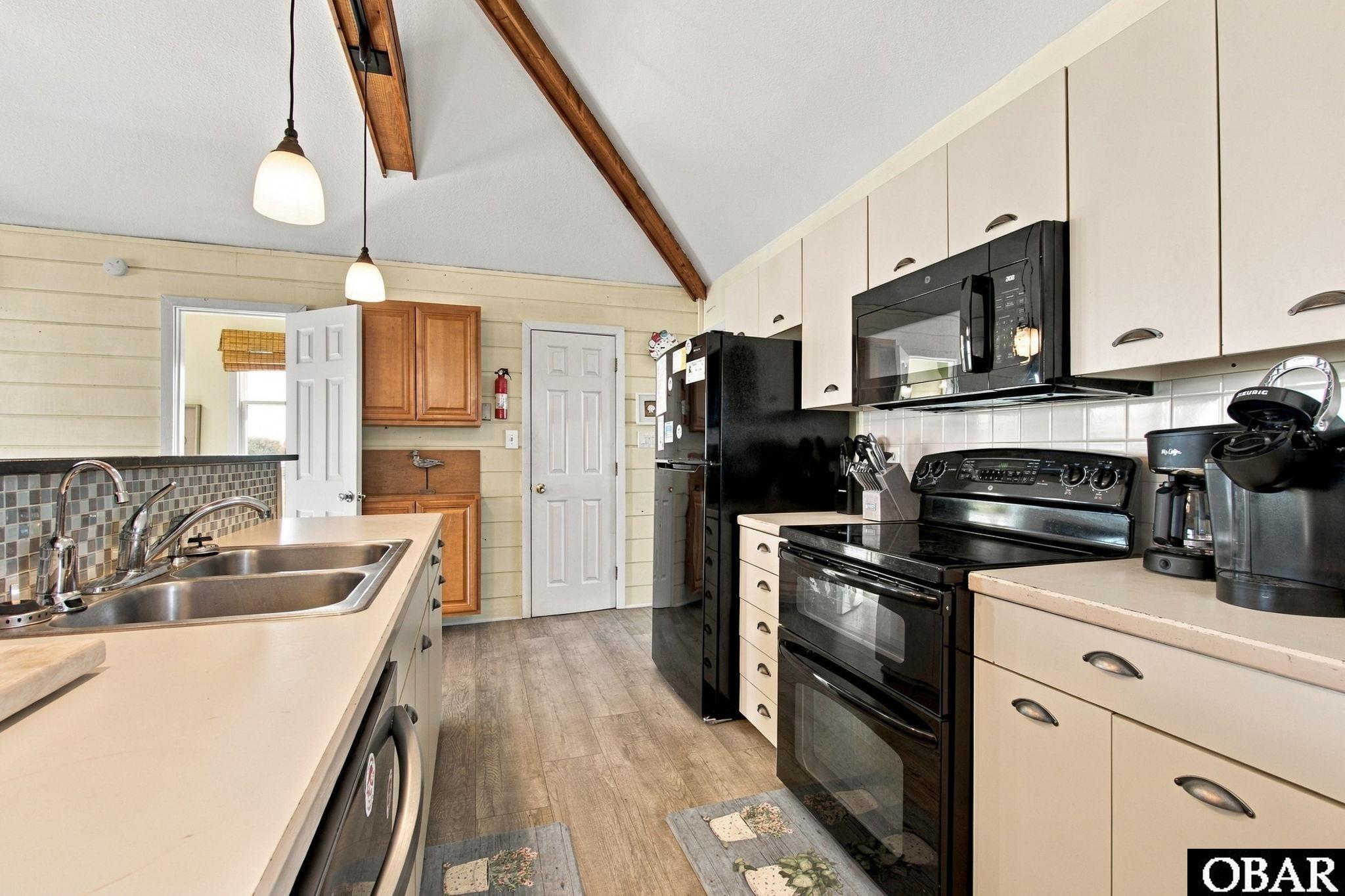 Kitchen with vaulted ceiling, exposed wooden beams, cream cabinets, and black appliances.