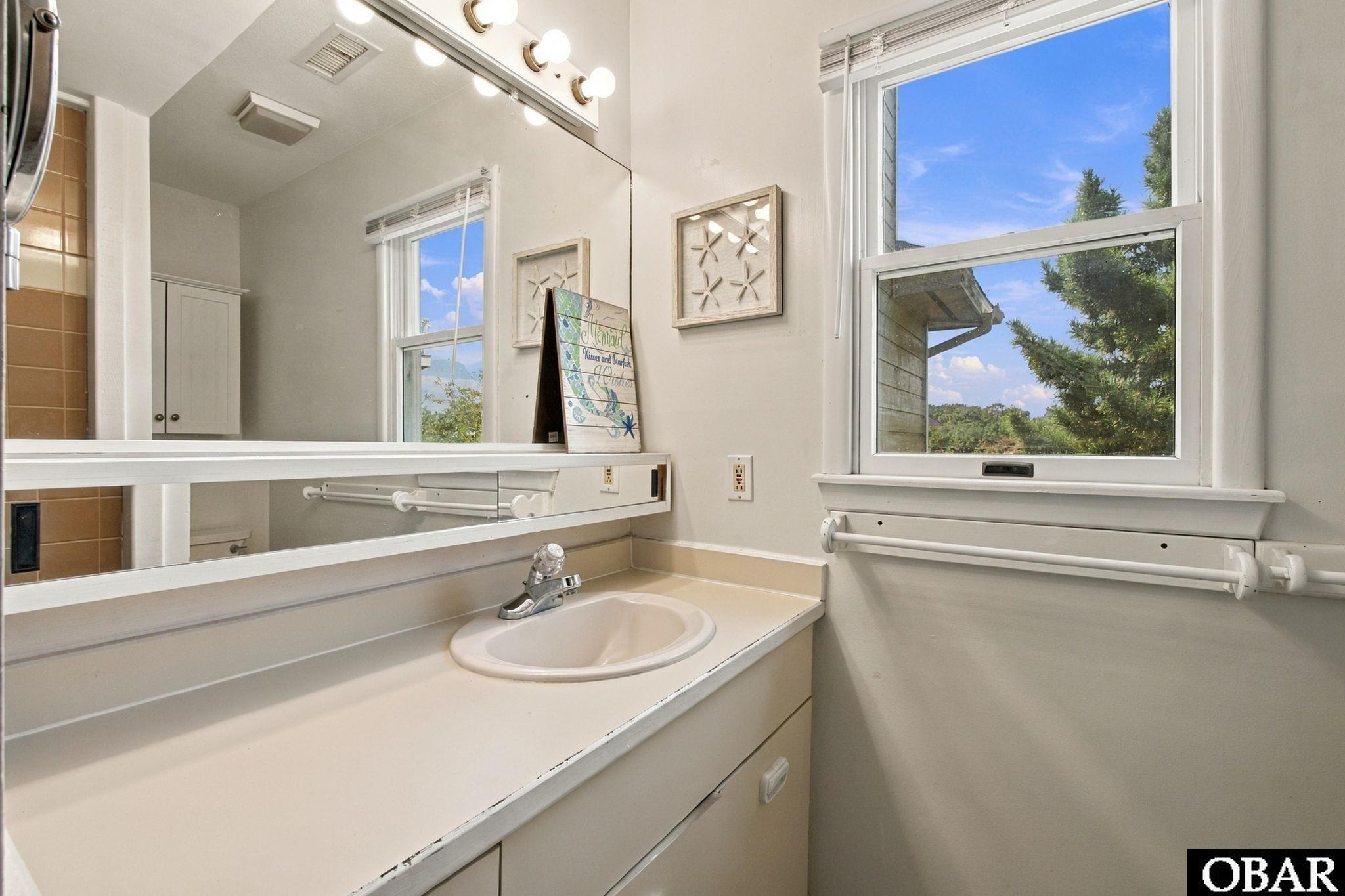 Bathroom vanity with an oval sink, large mirror, and window overlooking trees.