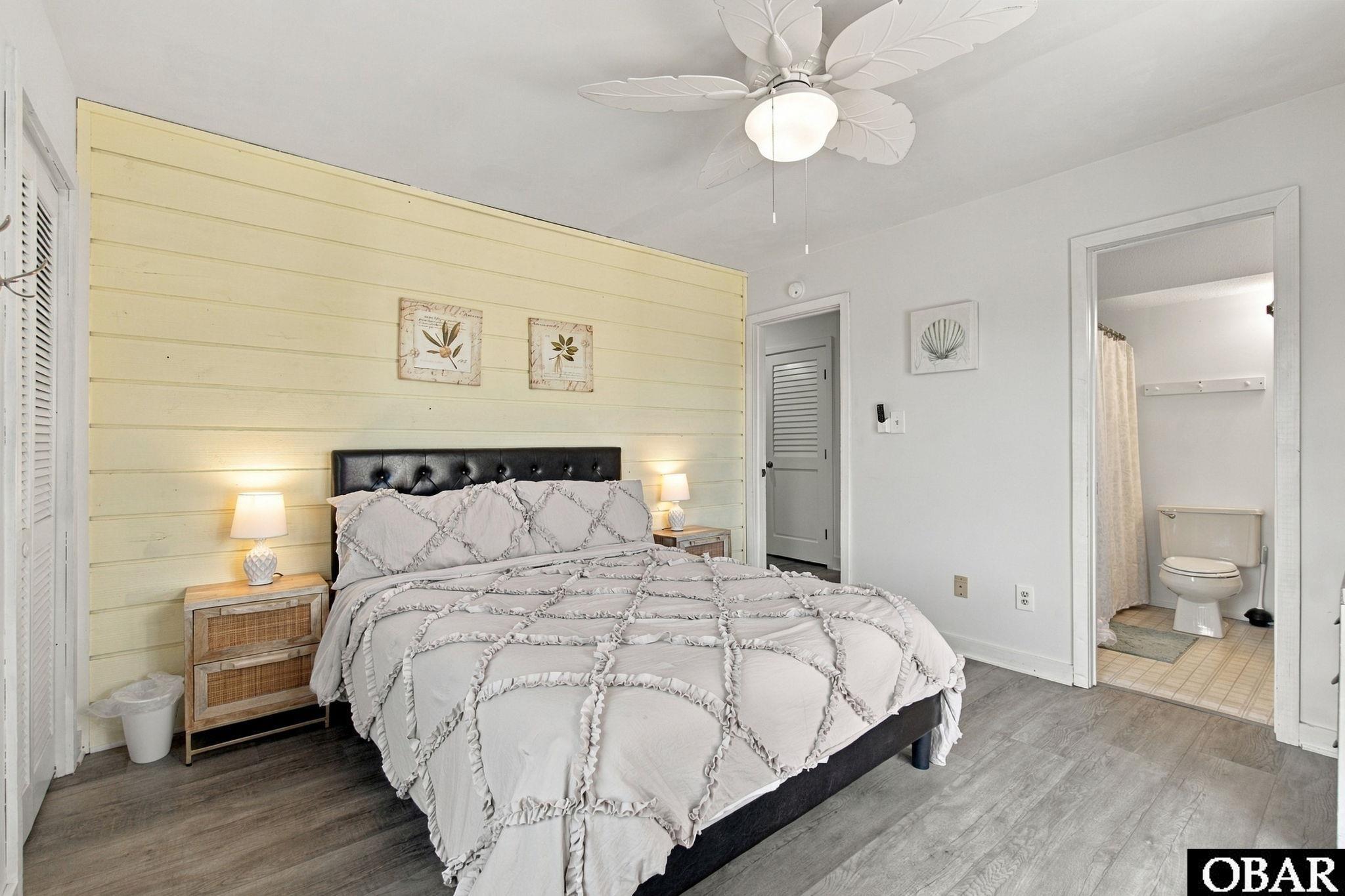 Bedroom with a large white ruffled bed against a pale yellow plank accent wall.