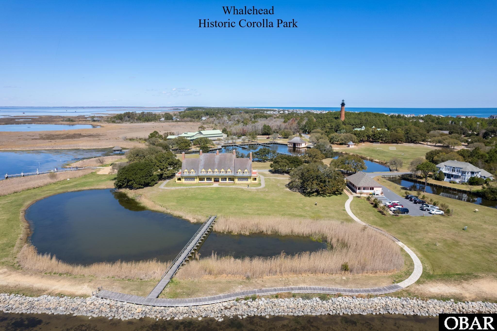 Aerial view of Whalehead Historic Corolla Park, with ponds, marshland, boardwalks, and a lighthouse beyond.