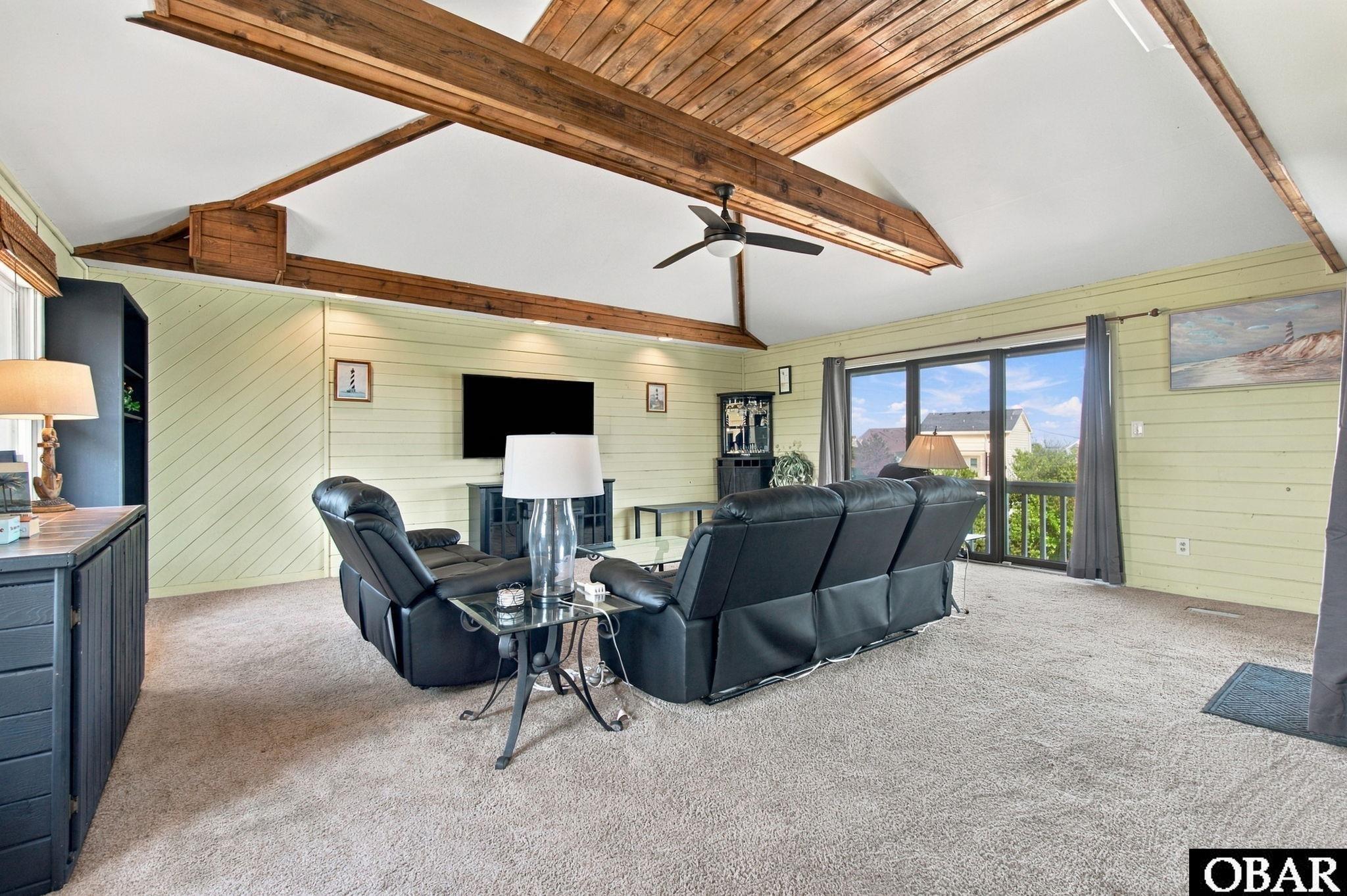 Furnished living room with exposed wood ceiling beams, black leather seating, and sliding doors to a balcony.