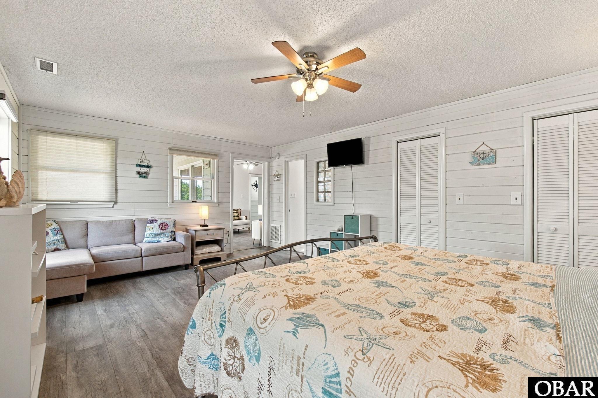 Bedroom with a seashell-patterned quilt, gray sofa, and white shiplap walls.