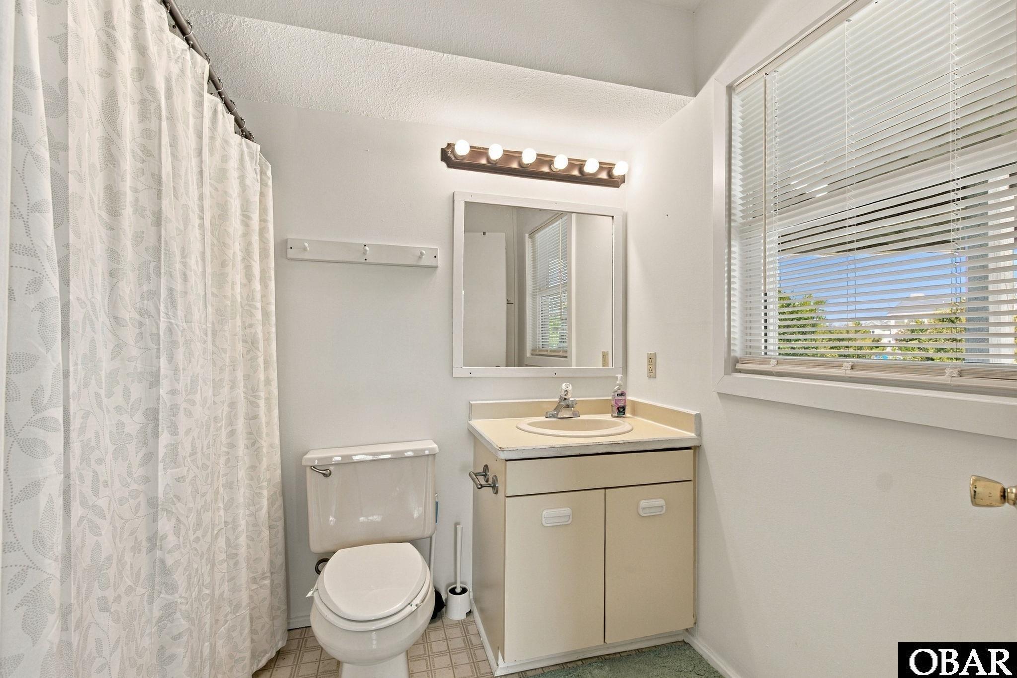 Bathroom with a beige vanity and window blinds beside a patterned shower curtain.