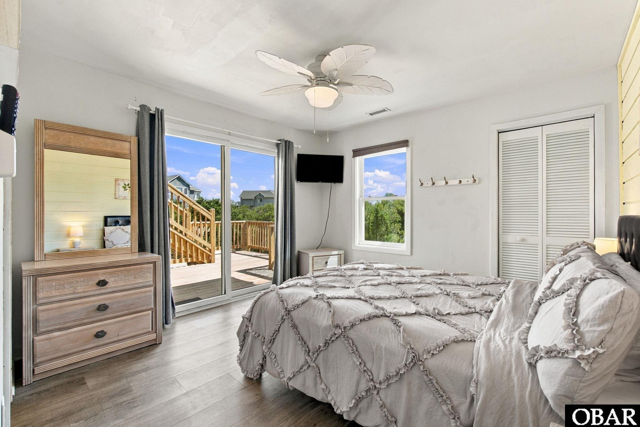 Bedroom with a large bed and dresser, opening onto a wooden deck through sliding glass doors.