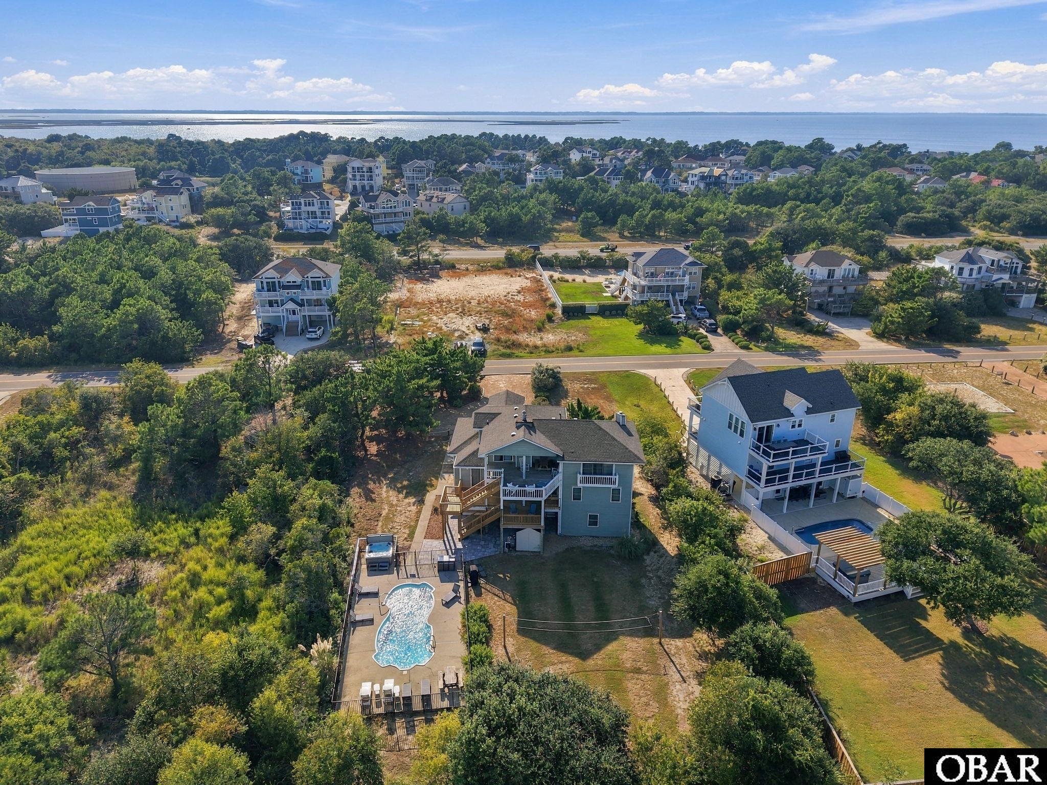 Aerial view of a vacant lot among coastal homes, with pools and water visible in the distance.