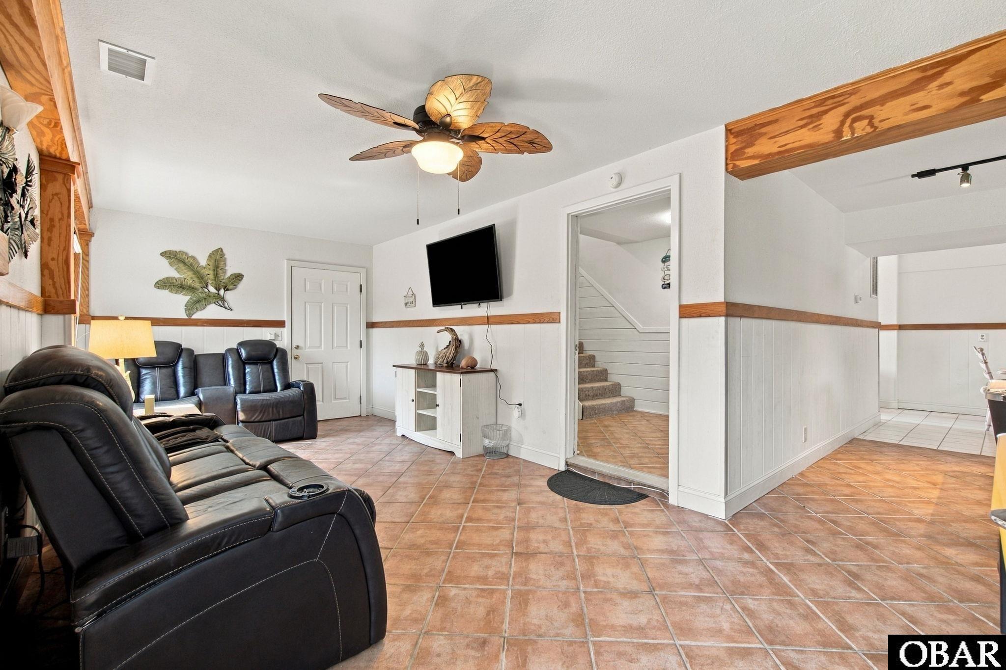 Living room with black leather recliners, terracotta tile floors, and a leaf-shaped ceiling fan.