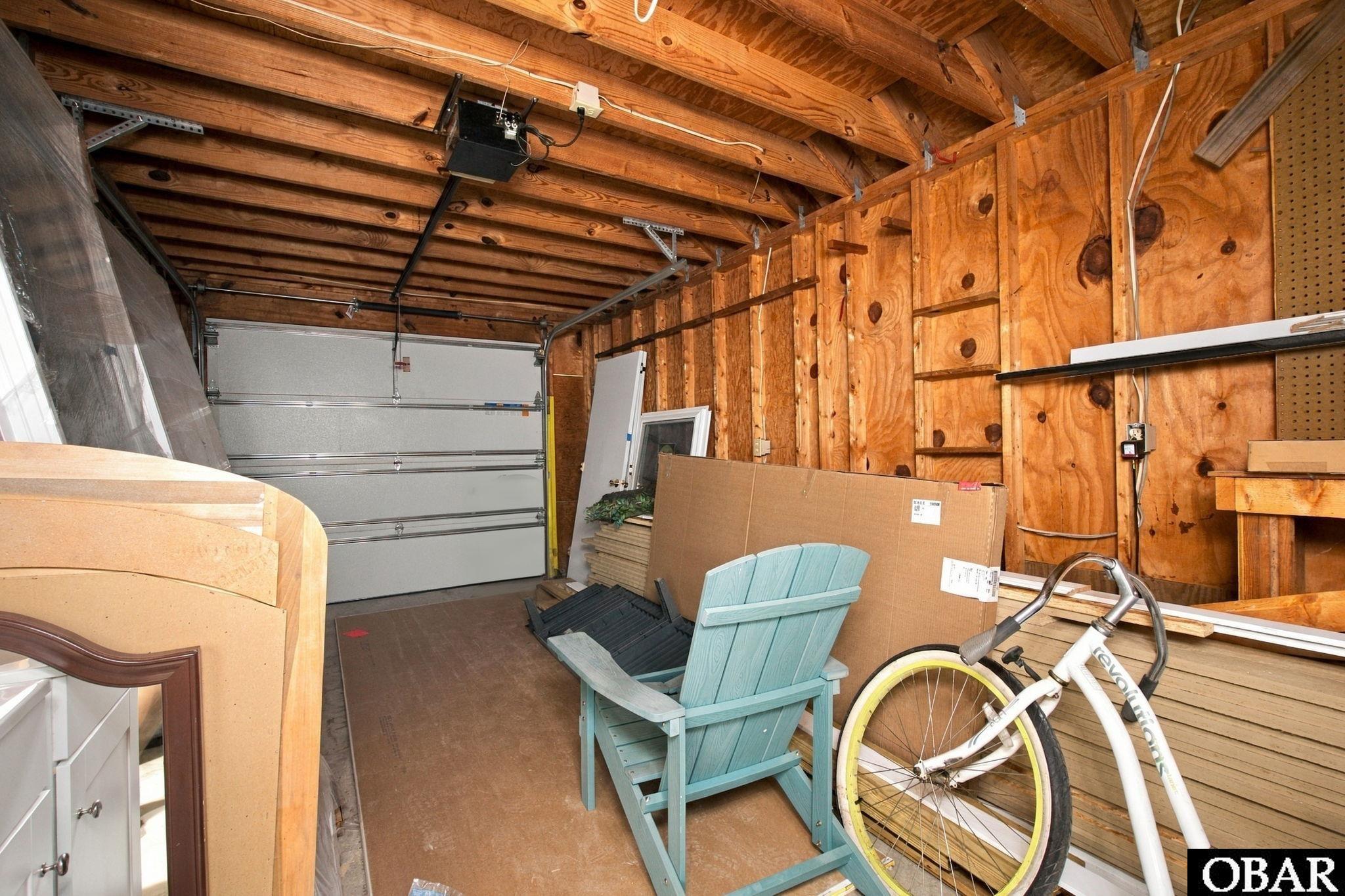 Garage with exposed plywood walls, stored materials, a turquoise chair, and a white bicycle.