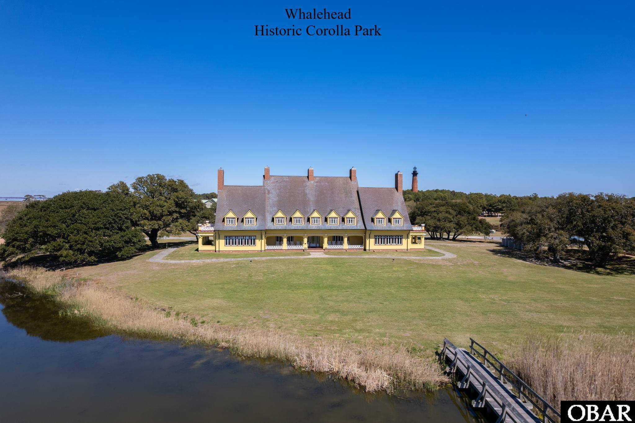Whalehead historic building beside a waterway, with a wooden footbridge and lighthouse in the background.