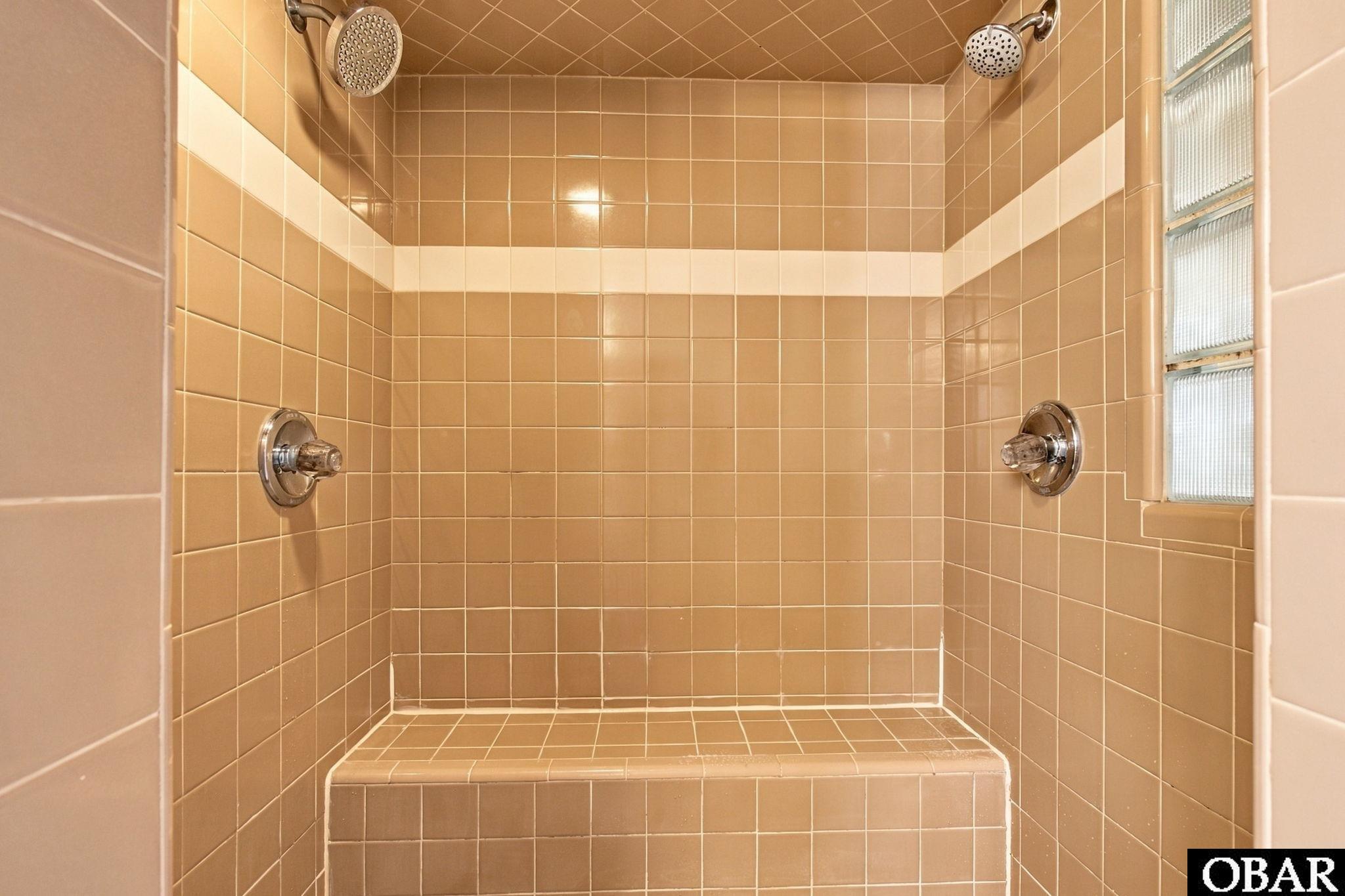Tan tiled walk-in shower with two showerheads, a built-in bench, and a glass-block window.