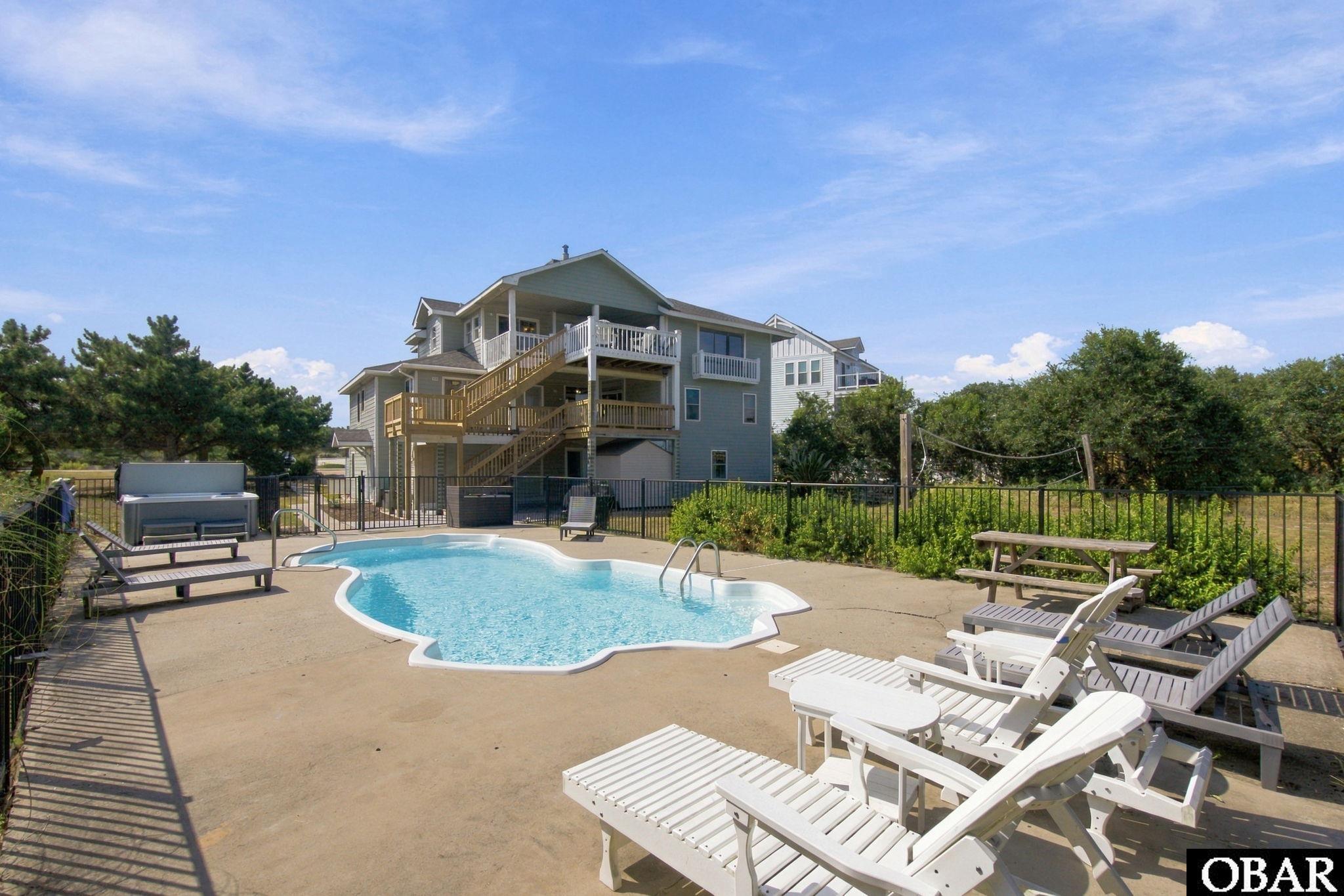 Home with a fenced swimming pool, white lounge chairs, and multi-level decks.