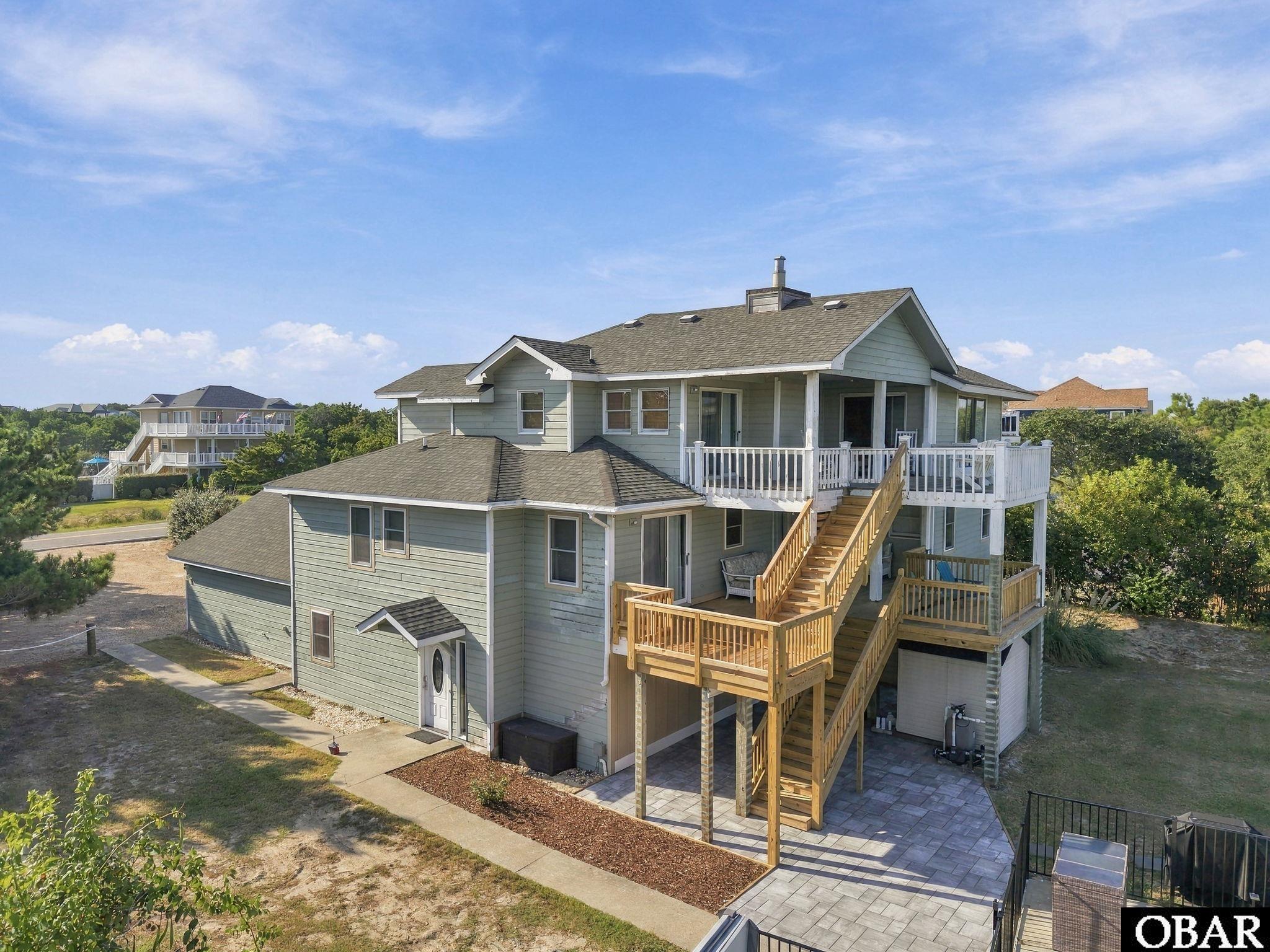 Gray-sided home with multiple wooden decks, exterior stairs, and a paved patio.