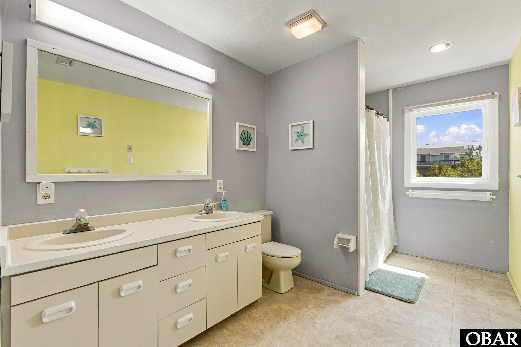 Bathroom with a double-sink vanity, large mirror, and curtained tub or shower area.