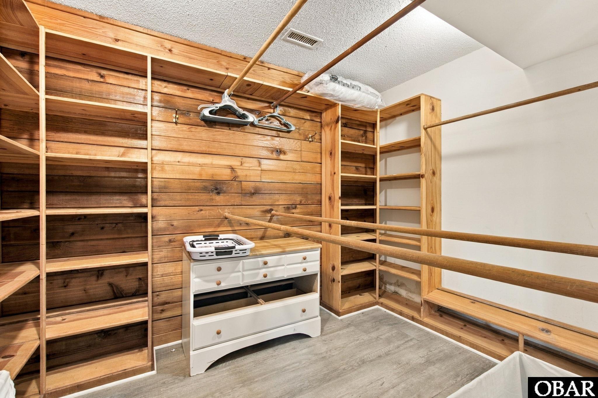 Walk-in closet with wood shelving and hanging rods surrounding a white chest of drawers.
