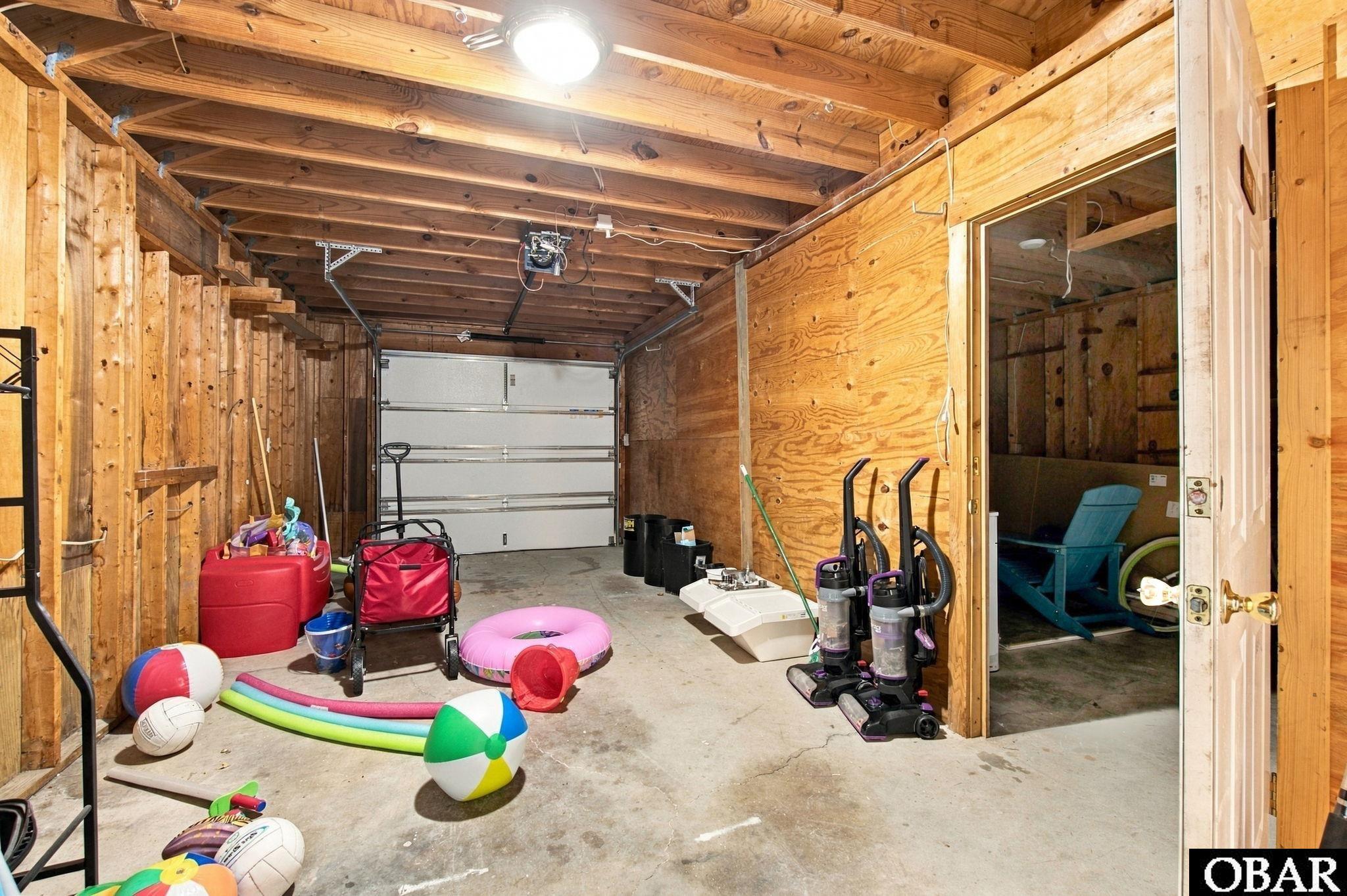 Wood-framed garage with exposed joists, a closed garage door, and beach toys and cleaning equipment in storage.