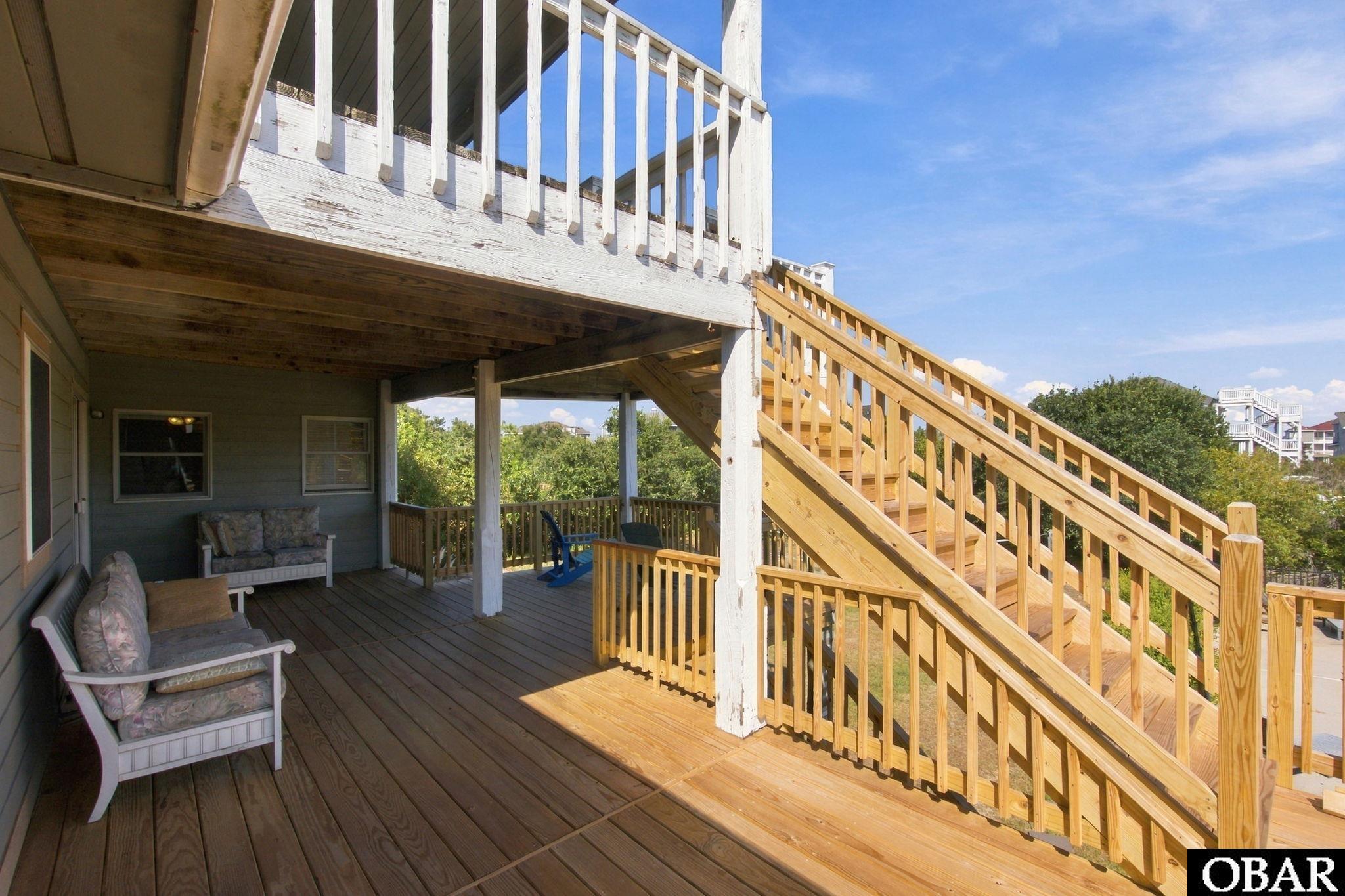 Covered wooden deck with porch seating and a long staircase to the upper balcony.