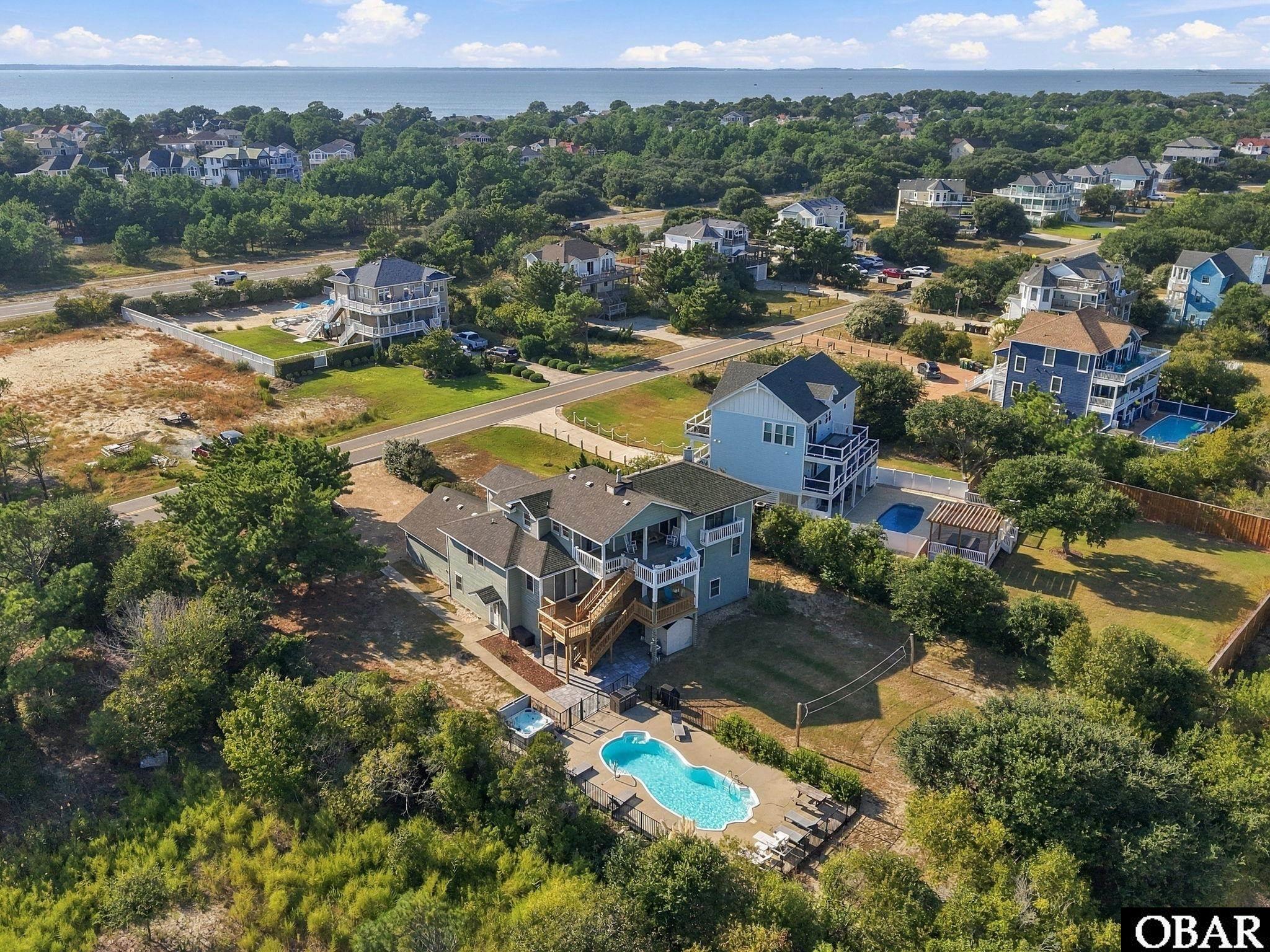 Aerial view of a coastal home with a private pool, neighboring houses, and water in the distance.