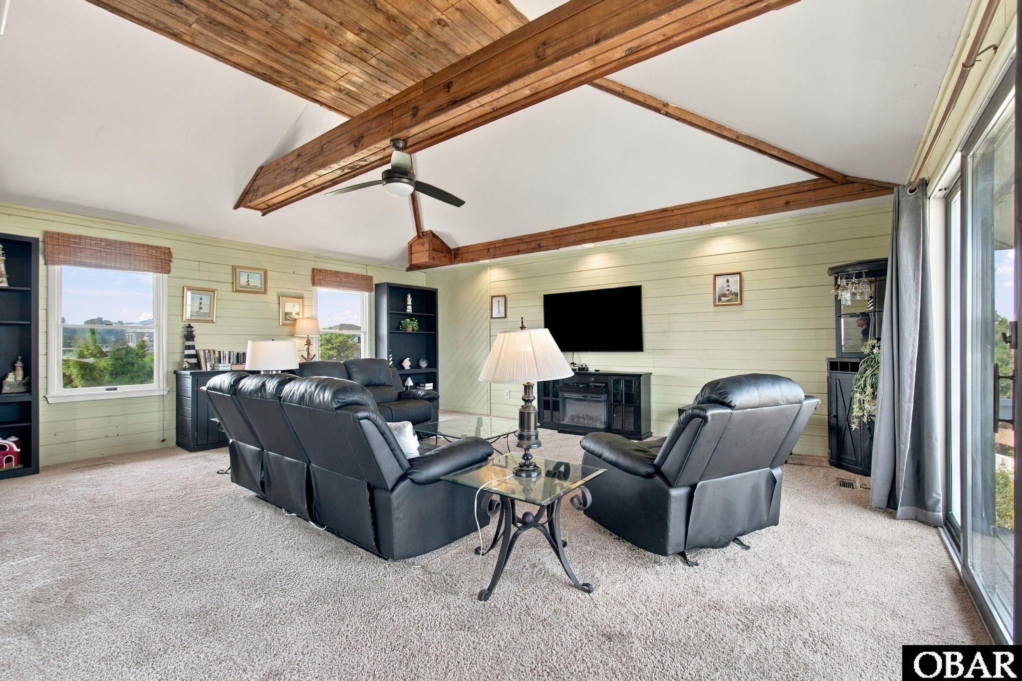 Living room with exposed wood ceiling beams, black leather seating, and sliding glass doors.
