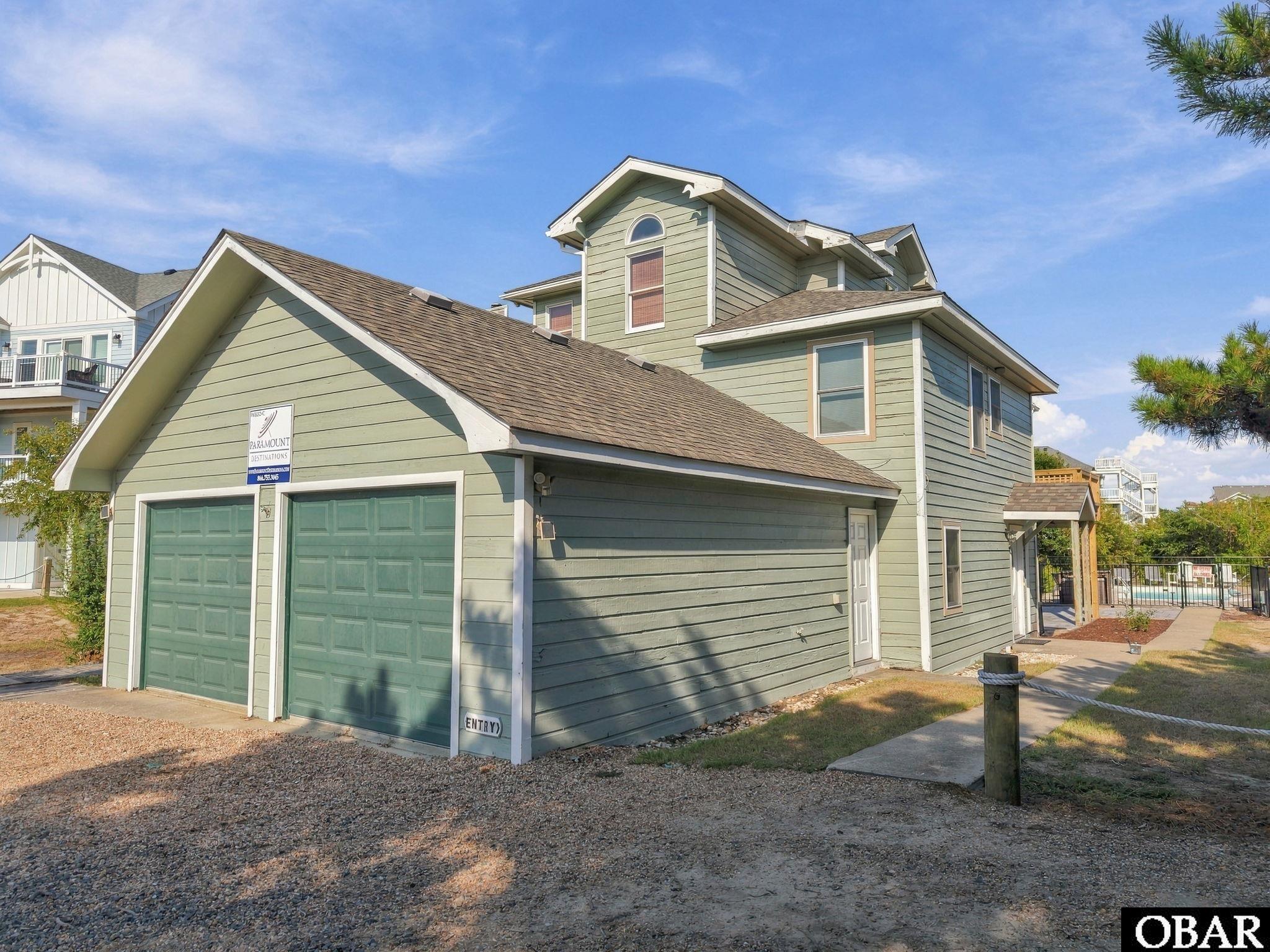 Green two-story house with white trim, two garage doors, and a covered walkway beside the yard.