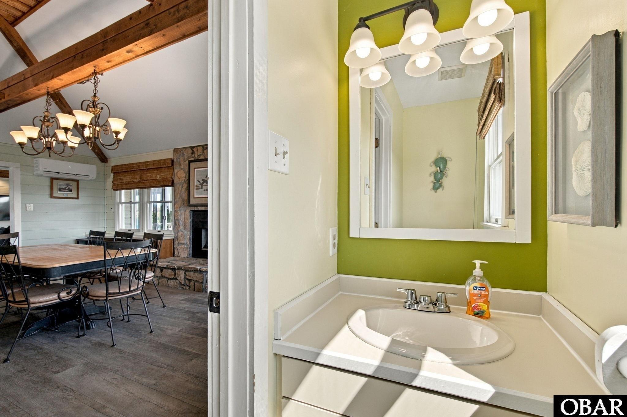 Bathroom vanity with a lime-green accent wall, overlooking a dining area with exposed wood beams.