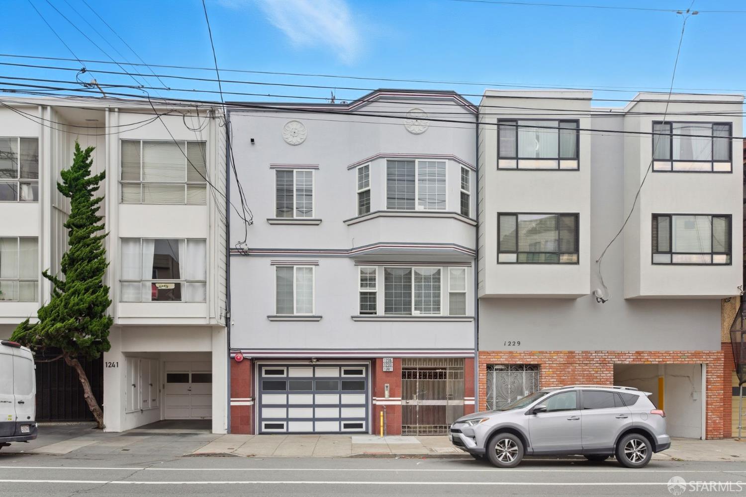 San Francisco apartment buildings with bay windows, a ground-level garage, and a silver SUV at the curb.