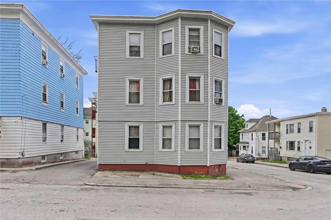 Gray three-story corner building with a bay facade and red-painted foundation.