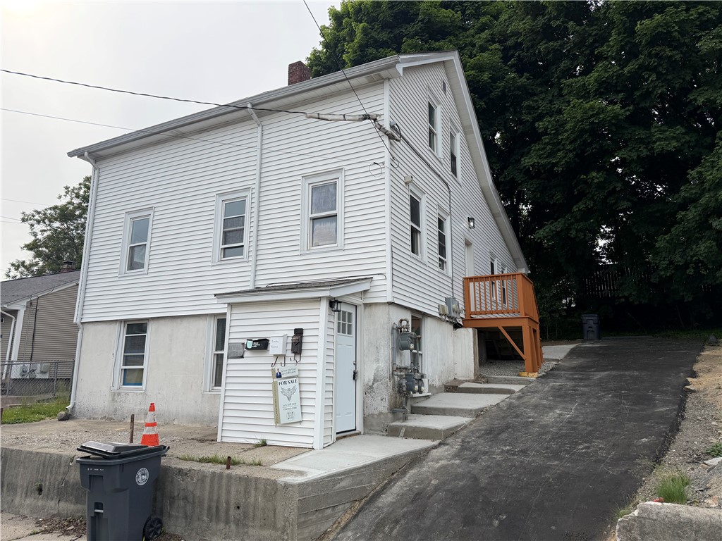 White two-story house with vinyl siding, a small wooden deck, and a paved driveway.