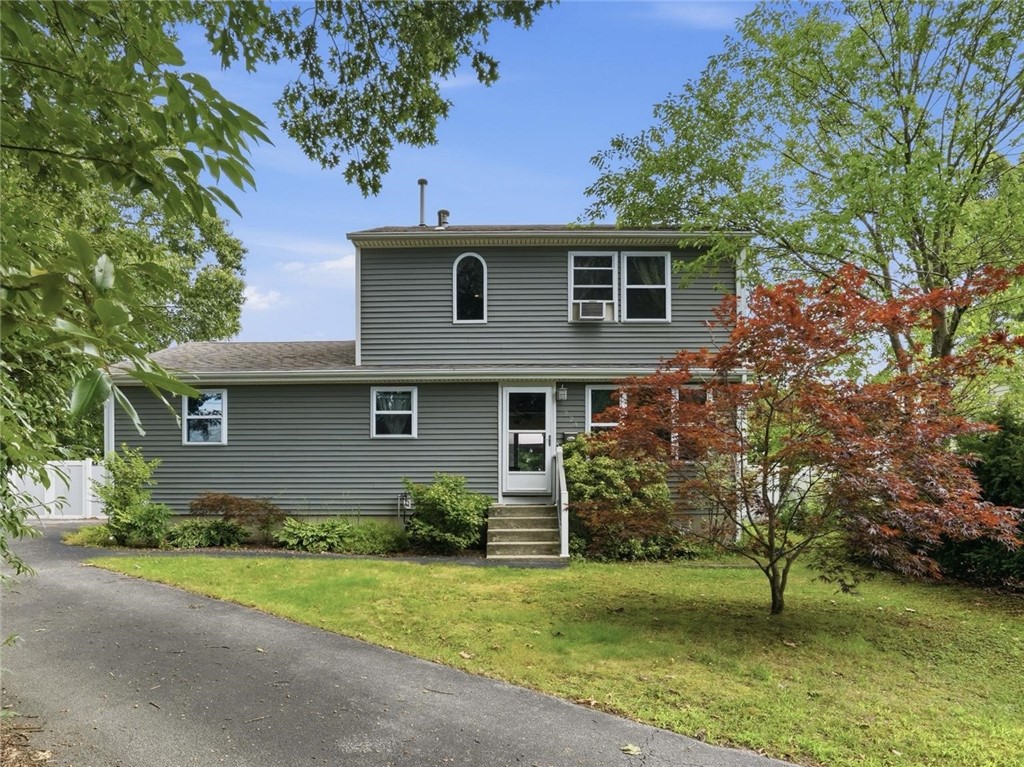 Gray two-story house with horizontal siding, a side entrance, and mature trees around the lawn.