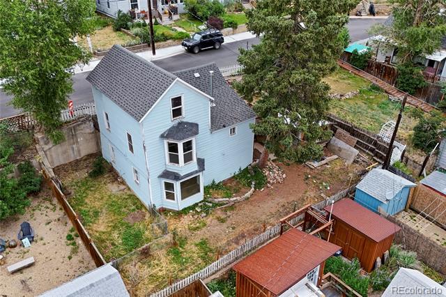 Light blue two-story house with a fenced yard and small outbuildings, seen from above.