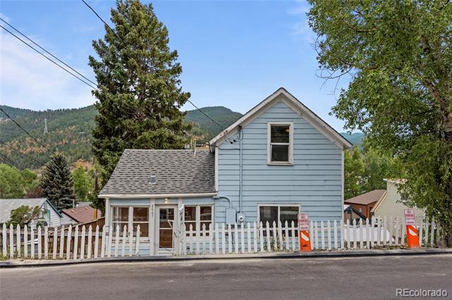 Light blue two-story house behind a white picket fence, with wooded hills in the background.