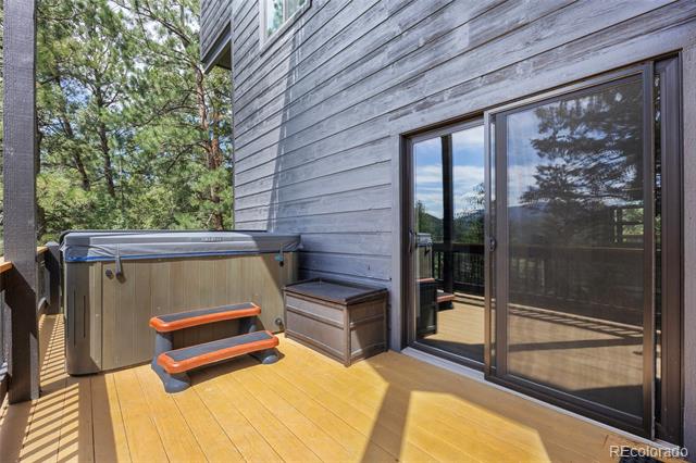 Wooden deck with a covered hot tub and sliding glass doors beside a gray-sided home.