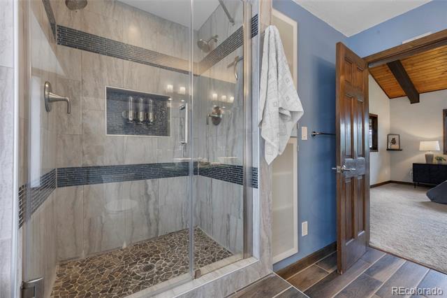Walk-in shower with glass doors, gray tile, dark accent bands, and a pebble floor.