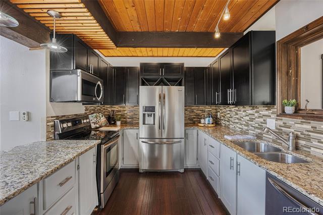 Kitchen with granite counters, stainless steel appliances, dark upper cabinets, and a wood plank ceiling.