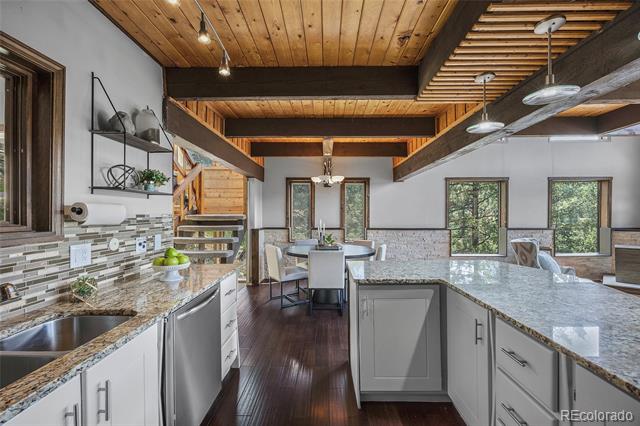 Open-plan kitchen with a large stone island, exposed timber beams, and forest views through the windows.