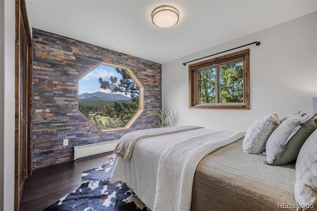 Bedroom with white bedding, a stone accent wall, and an octagonal window overlooking mountain scenery.