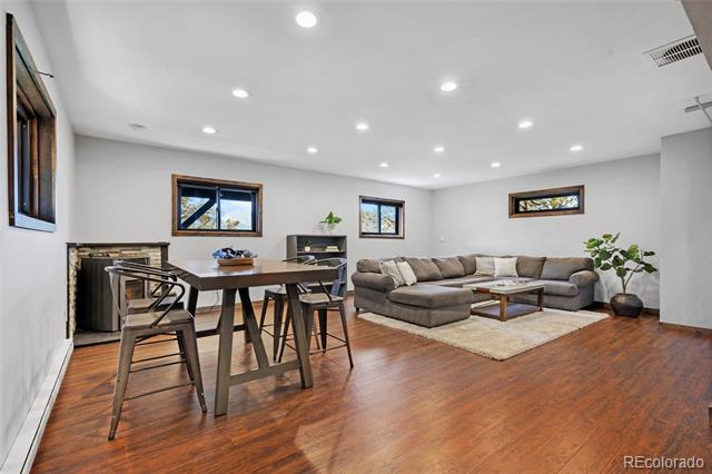Open living and dining room with a gray sectional, dining table, fireplace, and wood floors.