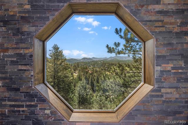Octagonal wood-framed window overlooking evergreen forest and distant mountains.