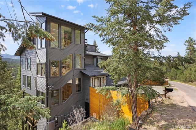 Modern multi-story home with gray siding and large windows among trees beside a driveway.
