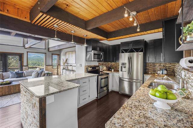 Open-plan kitchen with granite counters, dark cabinets, stainless appliances, and a vaulted wood ceiling.