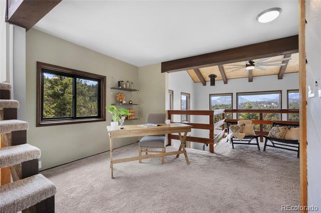 Home office with a wooden desk, adjoining sitting area, and mountain views through large windows.