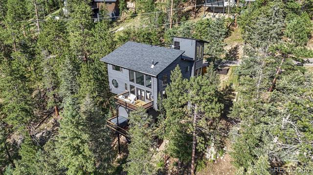 Modern gray house with an elevated deck nestled among evergreen trees.