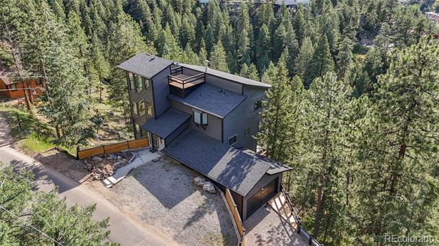 Aerial view of a modern dark-sided home surrounded by dense pine trees.