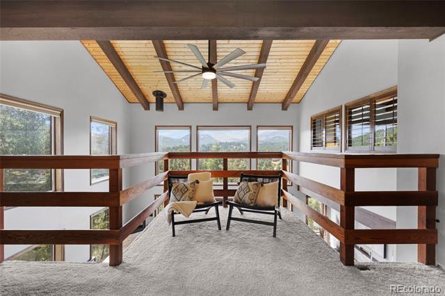 Loft sitting area with two chairs, exposed wood ceiling, dark railings, and mountain views through the windows.