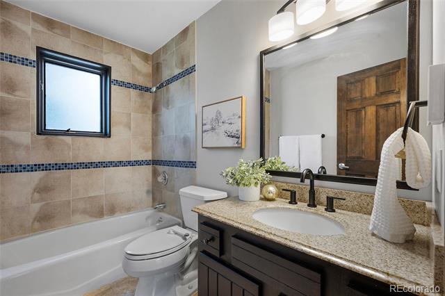 Bathroom with beige tile, blue mosaic accents, and a granite vanity beside a bathtub.