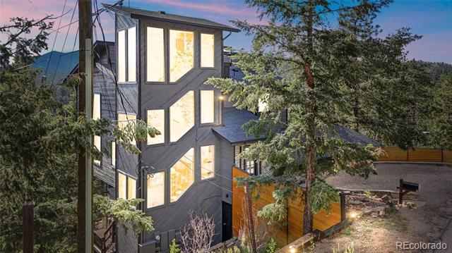 Modern multi-story home with angular design and illuminated windows among trees at dusk.